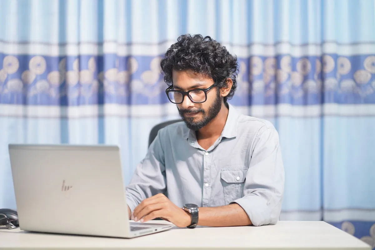 Jovem concentrado trabalhando em notebook em sala iluminada - Lovable ou Poupar AI para criar o site do negócio